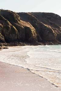 surfers on plemont beach in jersey step into the blue sea